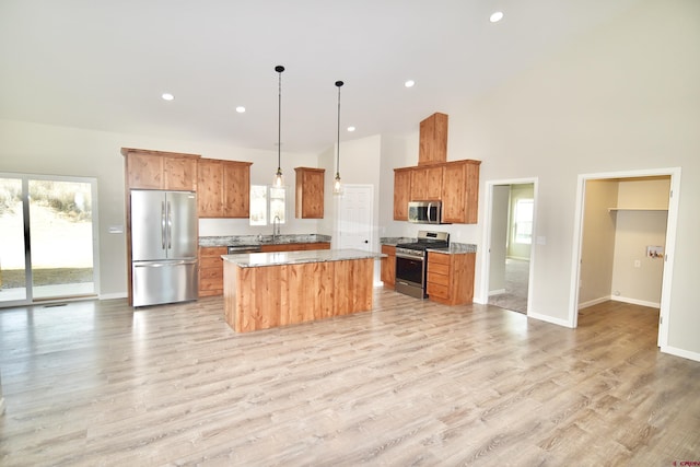 kitchen with light wood finished floors, brown cabinetry, a kitchen island, appliances with stainless steel finishes, and pendant lighting