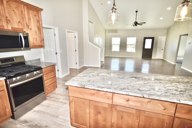 kitchen with stainless steel appliances, open floor plan, light stone counters, and a ceiling fan