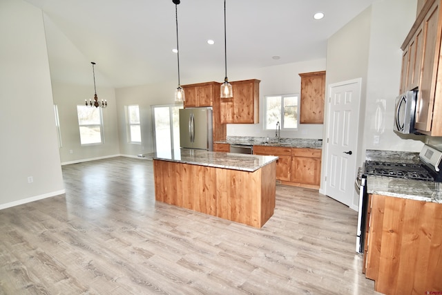 kitchen featuring stainless steel appliances, a sink, open floor plan, brown cabinetry, and decorative light fixtures