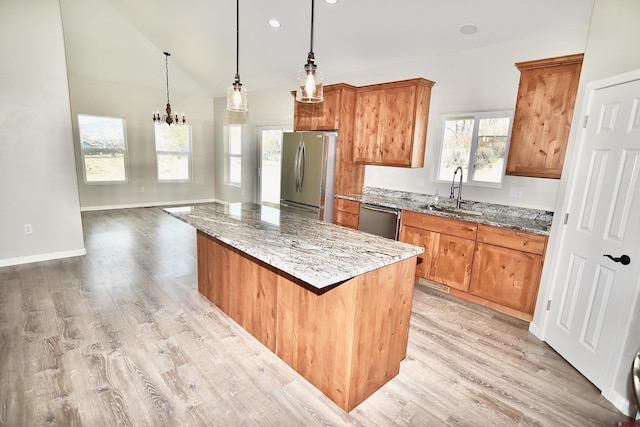 kitchen featuring stainless steel appliances, hanging light fixtures, stone countertops, a sink, and a kitchen island