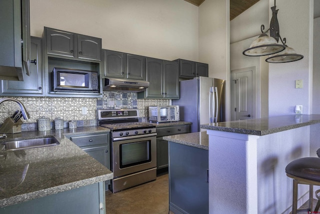 kitchen featuring under cabinet range hood, a sink, hanging light fixtures, appliances with stainless steel finishes, and dark countertops
