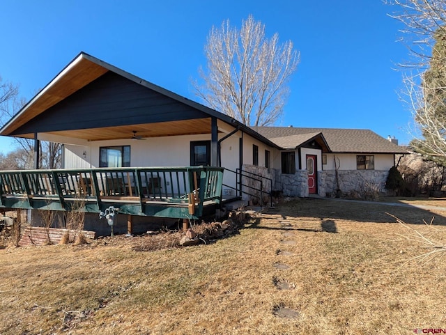 ranch-style house featuring stone siding, a deck, a front lawn, and a ceiling fan