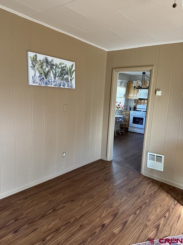 empty room featuring crown molding, visible vents, and dark wood-style flooring