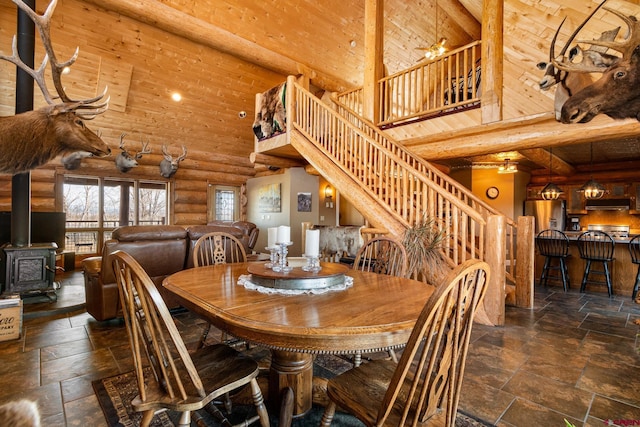 dining area with stone tile flooring, a towering ceiling, a wood stove, and stairs