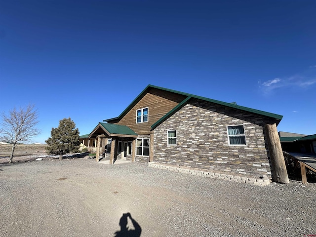 back of property featuring stone siding, metal roof, and a patio