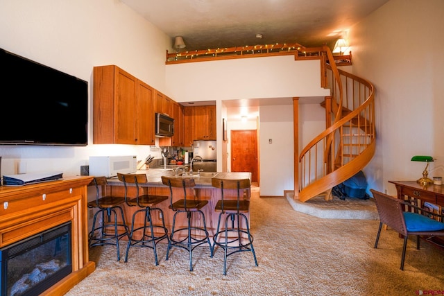 kitchen with brown cabinets, stainless steel microwave, white microwave, a peninsula, and a kitchen bar