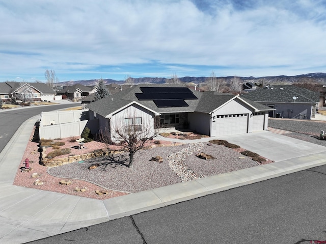 ranch-style home with driveway, a residential view, fence, roof mounted solar panels, and a mountain view