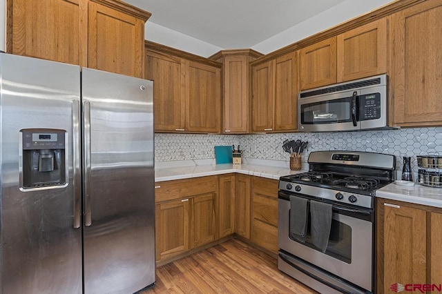 kitchen featuring stainless steel appliances, brown cabinetry, light countertops, and light wood-style flooring