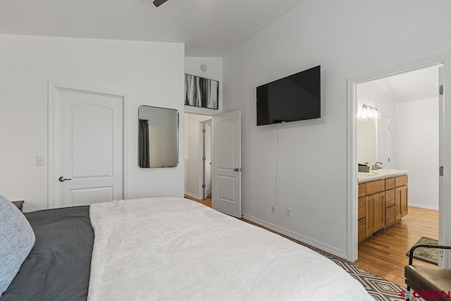 bedroom with light wood-style flooring, a sink, baseboards, vaulted ceiling, and ensuite bath