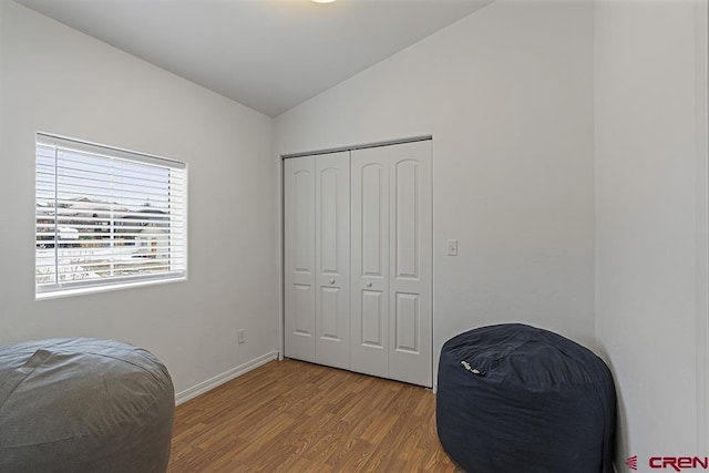 bedroom with lofted ceiling, light wood-style floors, baseboards, and a closet