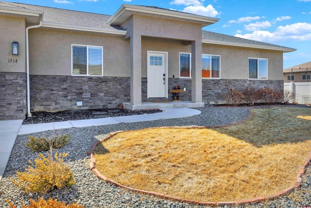 entrance to property with stone siding, roof with shingles, a yard, and stucco siding