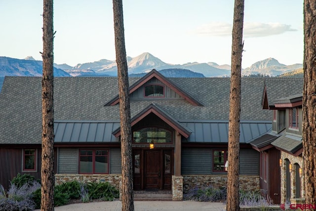 view of front facade featuring metal roof, a mountain view, a shingled roof, stone siding, and a standing seam roof