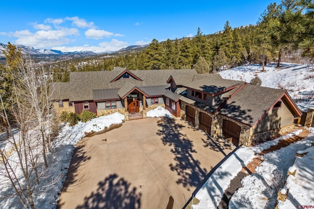 view of front of property featuring driveway, stone siding, metal roof, a standing seam roof, and a mountain view