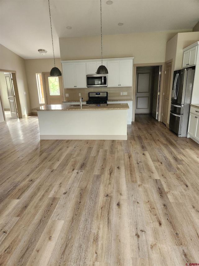 kitchen with decorative light fixtures, a center island with sink, appliances with stainless steel finishes, white cabinets, and light stone countertops