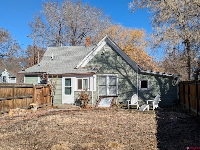 back of house with a fenced backyard, a chimney, a shingled roof, and a lawn