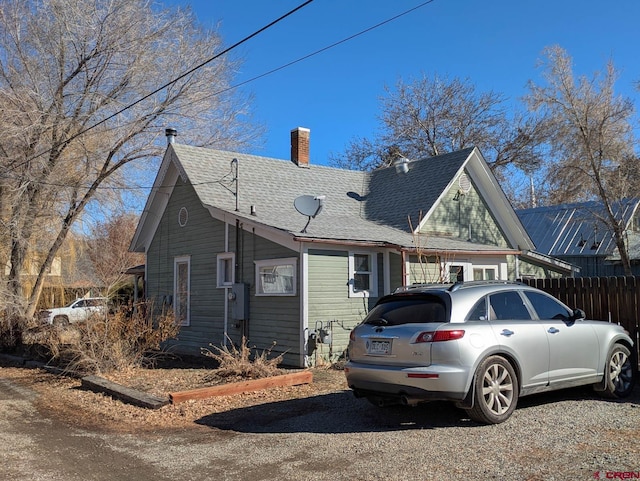 view of front of house with a chimney, fence, and roof with shingles