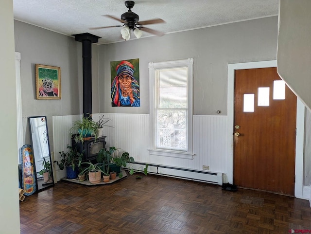 entrance foyer with a wood stove, a wainscoted wall, baseboard heating, and a textured ceiling