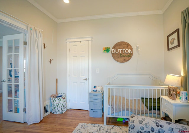 bedroom featuring a nursery area, ornamental molding, light wood-type flooring, and visible vents