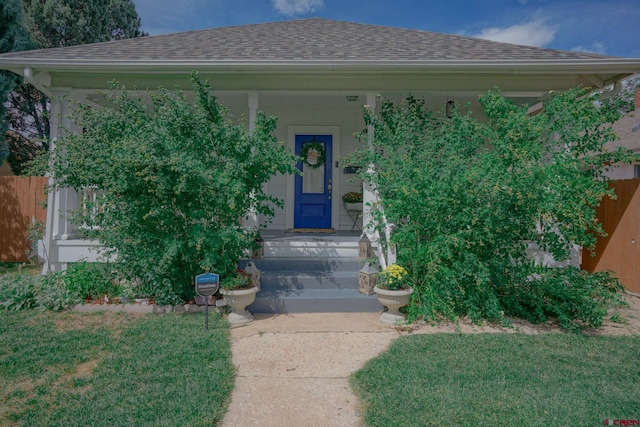 entrance to property with a shingled roof, fence, and a yard