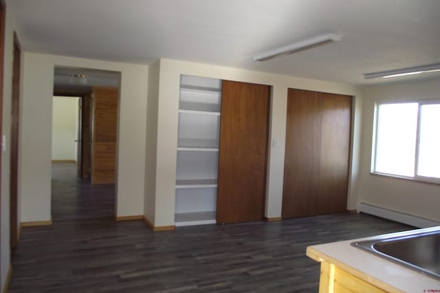 kitchen featuring light countertops, dark wood-type flooring, a baseboard heating unit, a sink, and baseboards