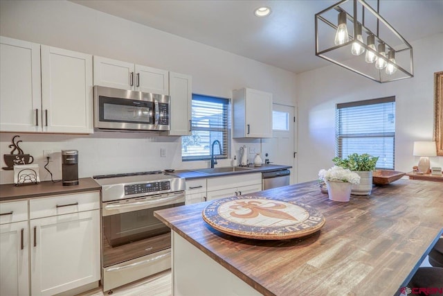 kitchen featuring butcher block counters, a sink, white cabinetry, hanging light fixtures, and appliances with stainless steel finishes