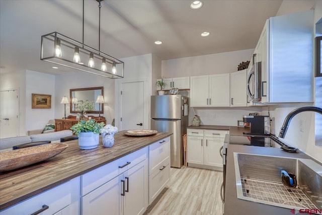 kitchen featuring white cabinets, open floor plan, wooden counters, appliances with stainless steel finishes, and hanging light fixtures