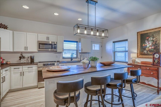 kitchen featuring stainless steel appliances, white cabinetry, a sink, a kitchen island, and butcher block countertops