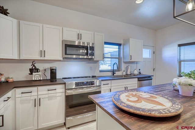 kitchen with appliances with stainless steel finishes, white cabinets, a sink, and wood counters