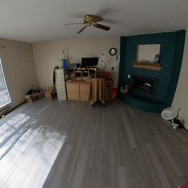 living area featuring a textured ceiling, a ceiling fan, a fireplace, and wood finished floors