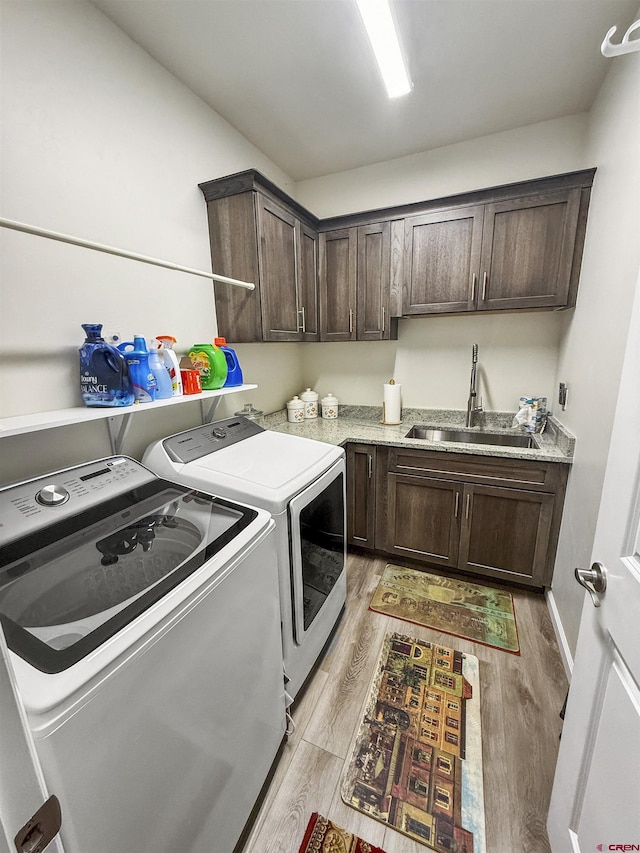 laundry area featuring cabinet space, a sink, light wood finished floors, and separate washer and dryer