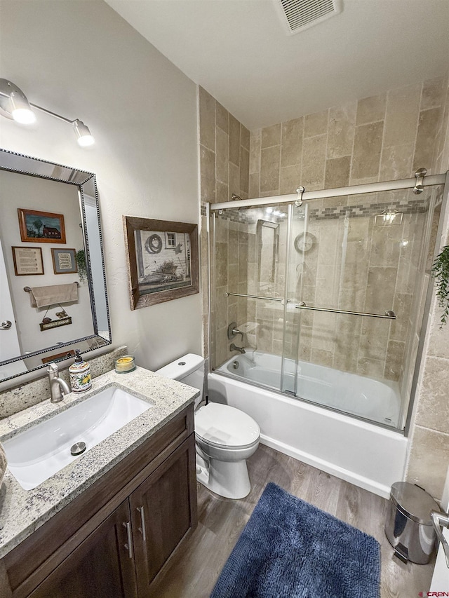 bathroom featuring enclosed tub / shower combo, toilet, wood finished floors, vanity, and visible vents