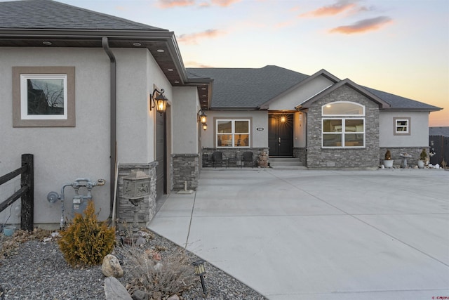 view of front facade with stone siding, roof with shingles, and stucco siding