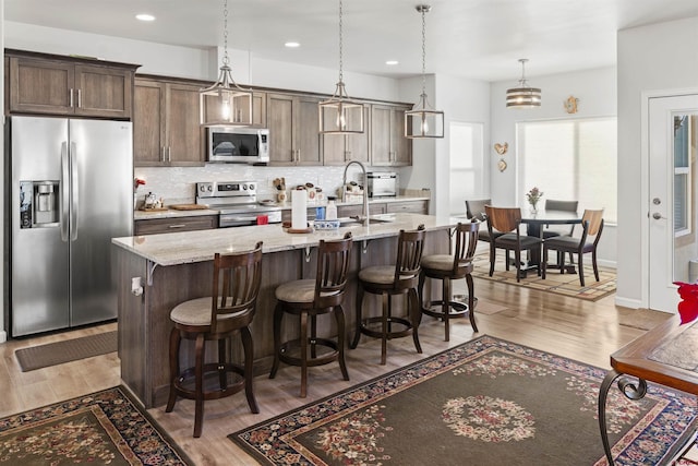 kitchen featuring a center island with sink, light wood finished floors, stainless steel appliances, tasteful backsplash, and a kitchen bar