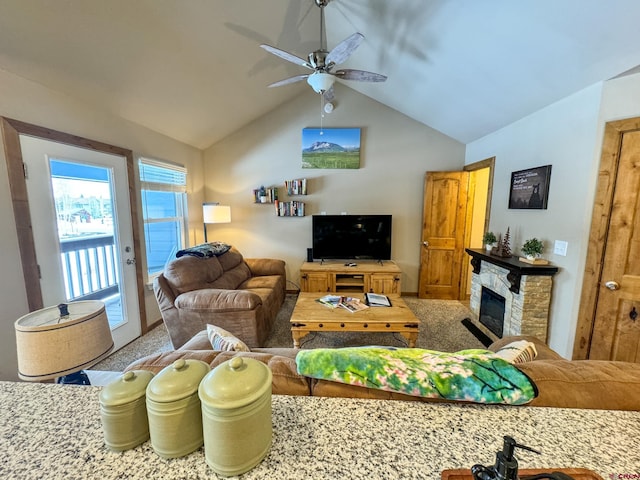 living room featuring lofted ceiling, carpet, a stone fireplace, and a ceiling fan