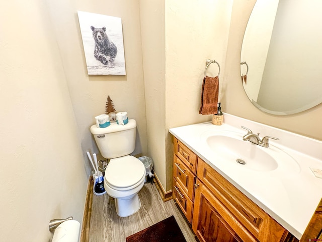 half bathroom with toilet, wood finished floors, and vanity