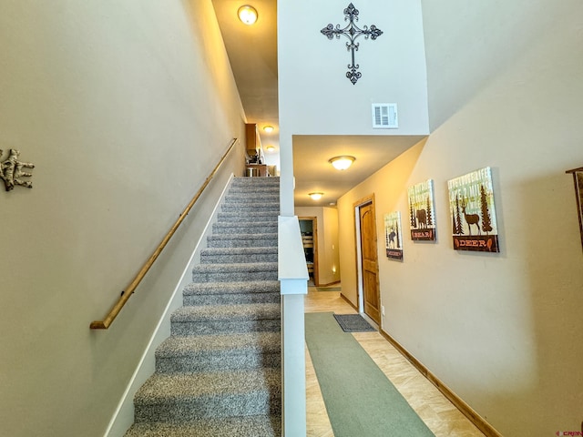 staircase with a high ceiling, visible vents, and baseboards