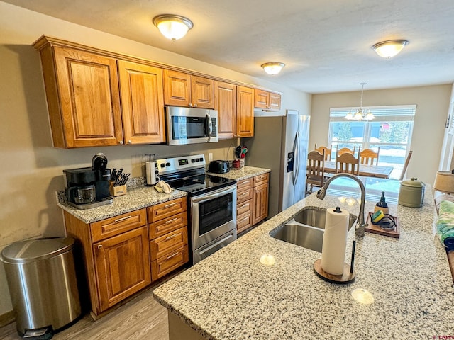 kitchen with appliances with stainless steel finishes, a sink, light stone counters, and brown cabinets