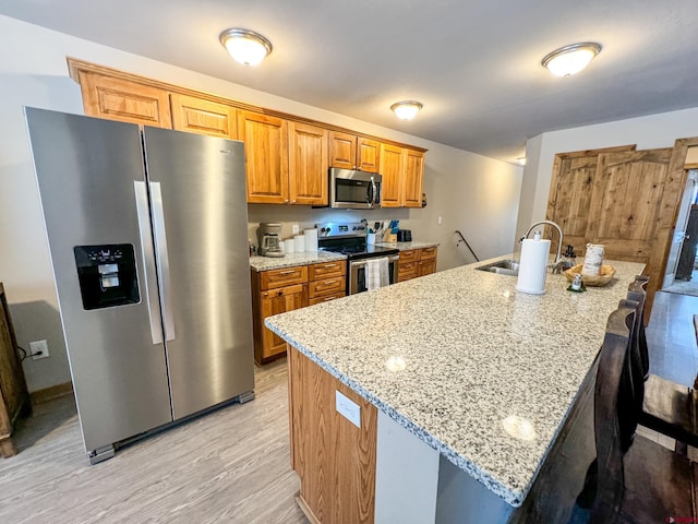 kitchen with light stone countertops, a sink, appliances with stainless steel finishes, brown cabinets, and light wood finished floors