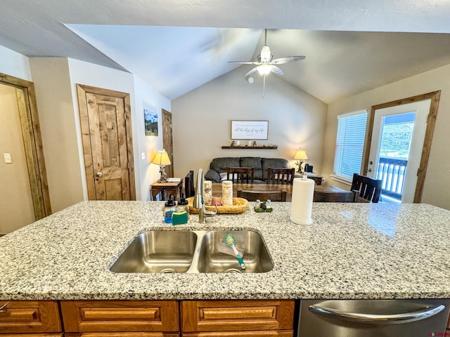 kitchen with dishwasher, light stone counters, open floor plan, and a sink