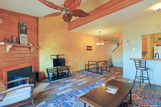 living area with ceiling fan with notable chandelier, a fireplace, wood finished floors, and beam ceiling