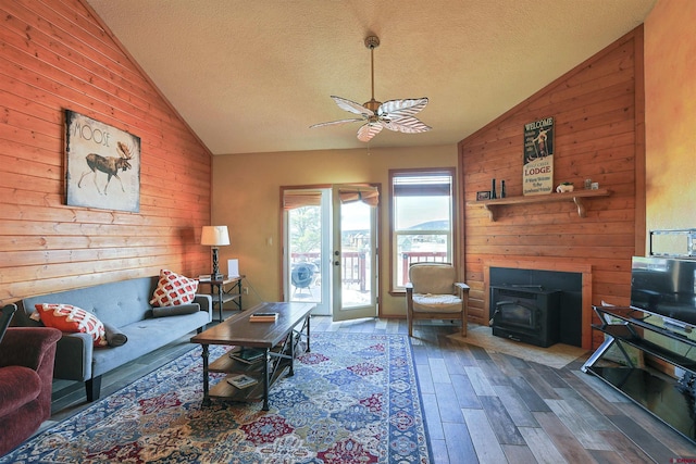 living area with a textured ceiling, wood walls, wood finished floors, and a wood stove