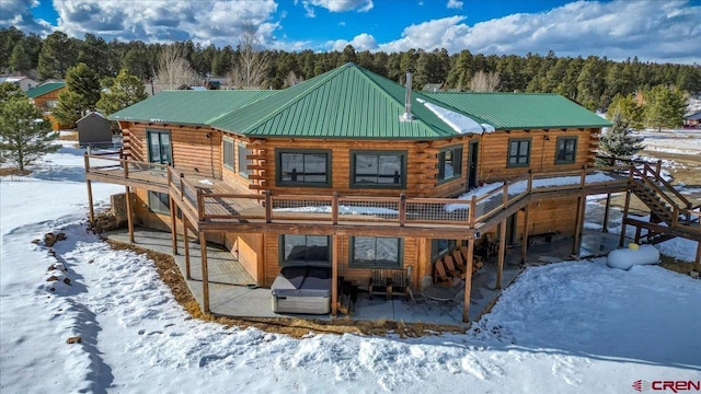 snow covered house featuring metal roof, a patio, and log siding