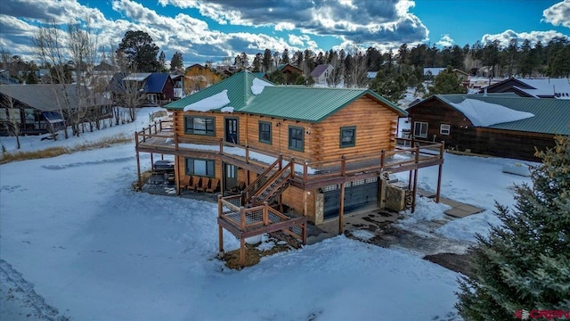 snow covered rear of property with a deck, metal roof, stairway, and log siding