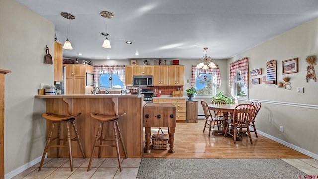 kitchen featuring a chandelier, a kitchen breakfast bar, appliances with stainless steel finishes, tasteful backsplash, and pendant lighting