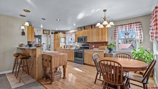 kitchen featuring hanging light fixtures, backsplash, stainless steel gas stove, light brown cabinets, and a peninsula