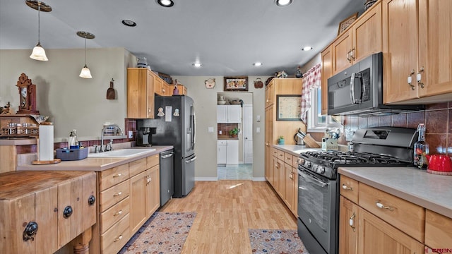 kitchen featuring light wood finished floors, appliances with stainless steel finishes, backsplash, and a sink