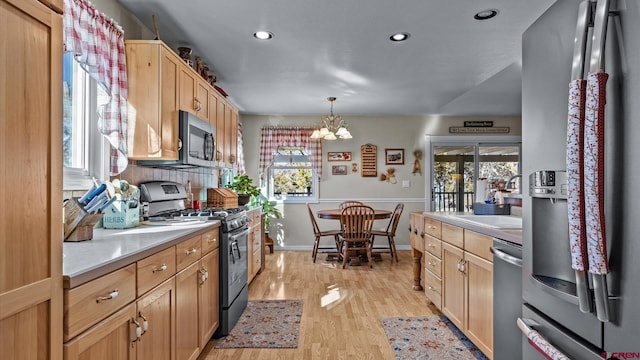 kitchen with stainless steel appliances, light countertops, light wood-style floors, and a notable chandelier