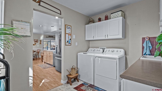 washroom featuring washer and dryer, cabinet space, and light wood-style flooring