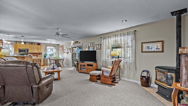 living area featuring light carpet, light tile patterned floors, baseboards, ceiling fan, and a wood stove