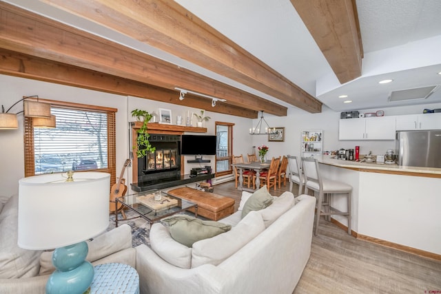 living room with a chandelier, a glass covered fireplace, beam ceiling, and baseboards